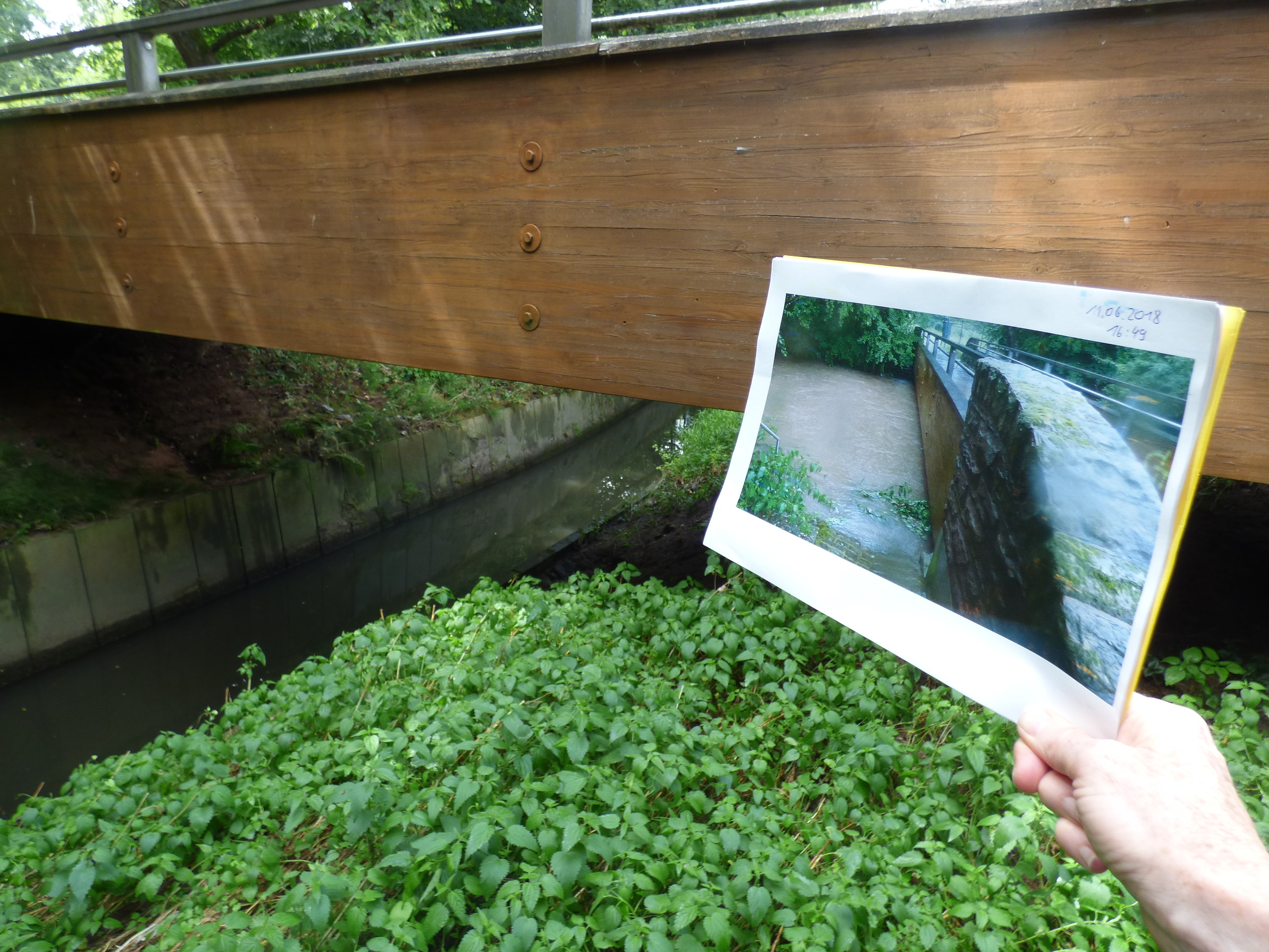 Das Bild zeigt die Radfahrer-/Fußgängerbrücke über die Lauter, rund 80 Meter nördlich der Autobahnbrücke. Im Bild zu sehen ist ein Foto derselben Stelle vom 11. Juni, 16.49 Uhr, als der Pegel der Lauter rund drei Meter höher stand und nahezu die Unterkante der Brücke erreichte.