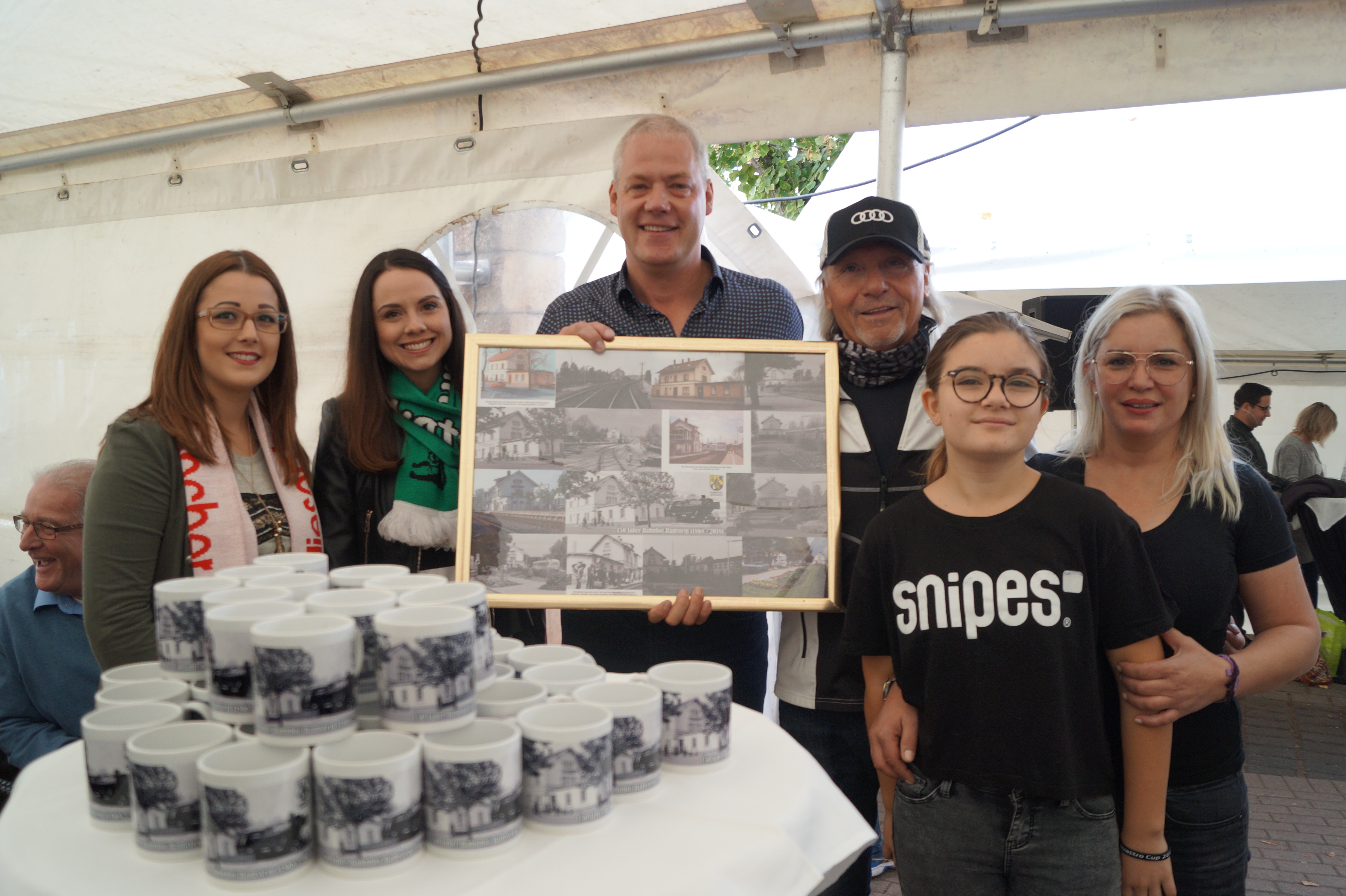 Bürgermeister Ralf Hechler (Mitte) überreichte Michael Blauth eine Bahnhofs-Collage als Dank für sein Engagement. Janine I. (l.) und Lena I. (2.v.l.) übernahmen den Verkauf der Jubiläumstassen für den guten Zweck