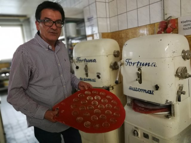 Horst Hartmuth an der Klievmaschine, wo Brötchen hergestellt werden. In der Hand ein Backblech, das für „Opa Philips Weck“ mit Schweineschmalz eingerieben wird. Foto: Kling