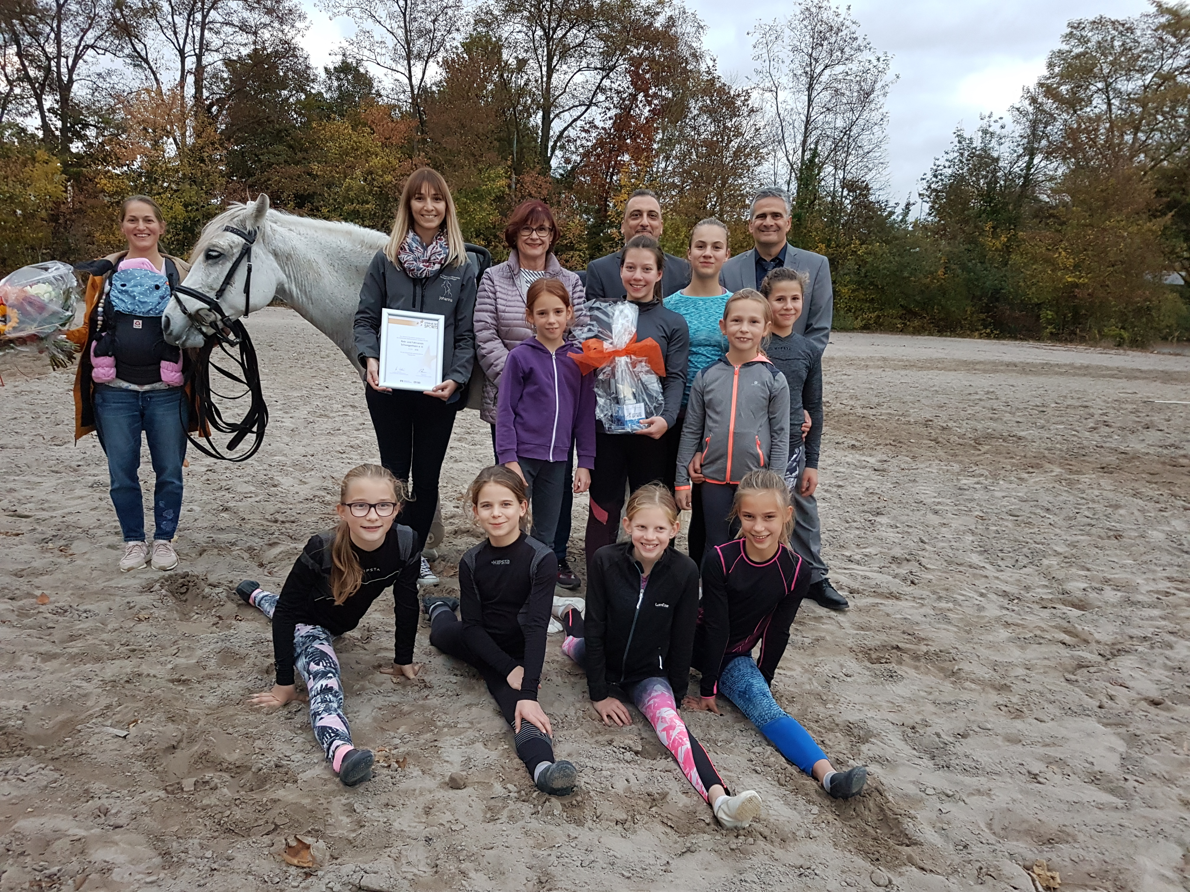 Offizielle Preisübergabe des Sterns in Bronze auf dem Trainingsgelände des Reit- und Fahrvereins Schwegenheim: (mit Urkunde) Johanna Patzelt (Voltigier-Trainerin), daneben in hinterer Reihe (v. l. n. r.): Elke Vollmar (1. Vorsitzende), Özgür Bardakci (Volksbank Kur- und Rheinpfalz, Regionaldirektor Lingenfeld), Thilo Heinrich (Volksbank Kur- und Rheinpfalz, Finanzberater Privatkunden Filiale Schwegenheim) sowie weitere Vereinsmitglieder und trainierende Kinder.