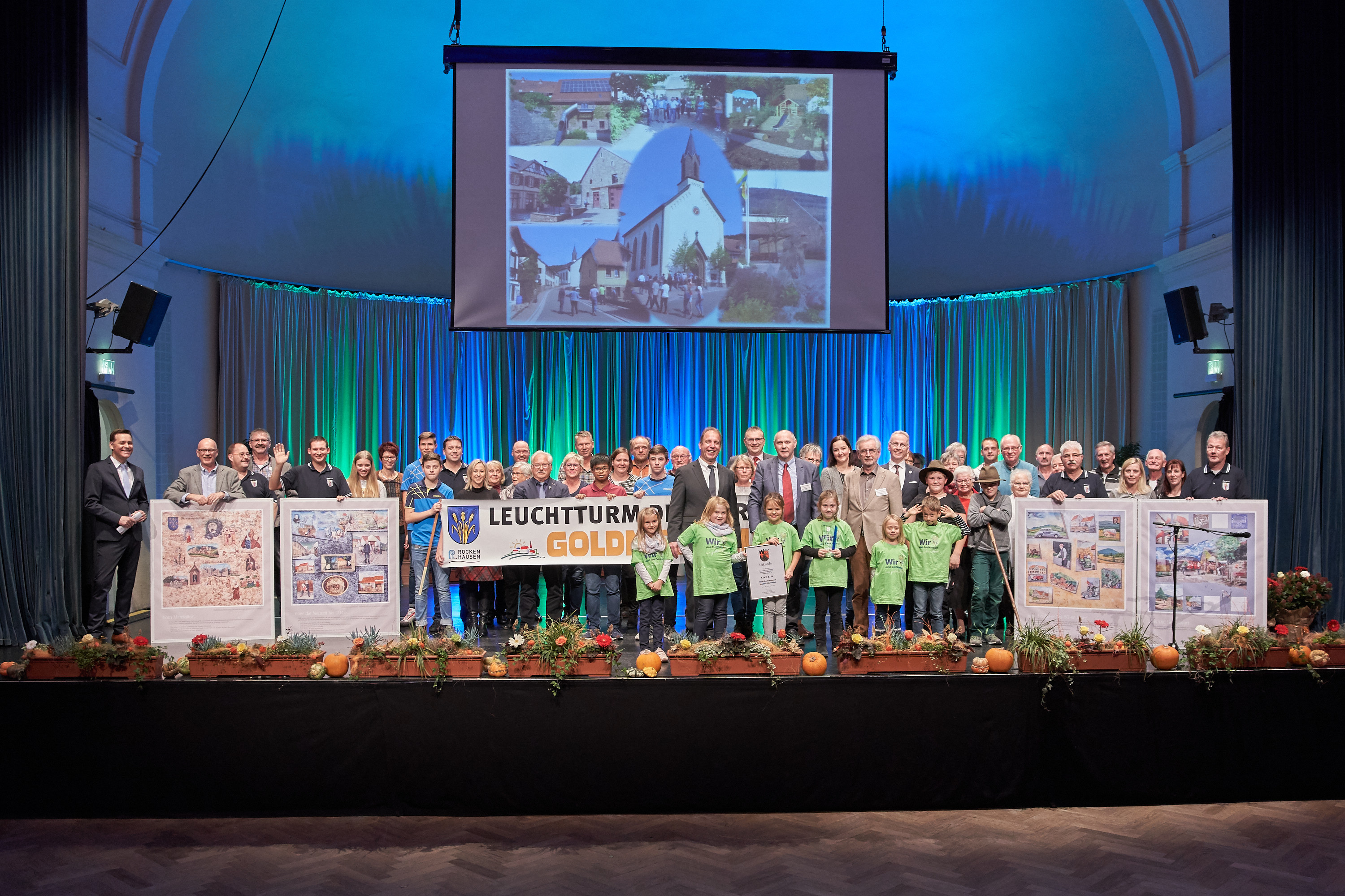 Die komplette Marienthaler Delegation nach der Auszeichnung. Links und rechts wurden jeweils zwei Epochen der gemalten Marienthaler Ortschronik präsentiert. In der Bildmitte sind die Marienthaler Kinder mit Urkunde und Pokal ganz vorne, direkt dahinter die Herren Innenstaatssekretär Stich, Verbandsbürgermeister Cullmann, Ortsvorsteher Bauer, Stadtbürgermeister Seebald und Landrat Guth, von links nach rechts. Foto: ps