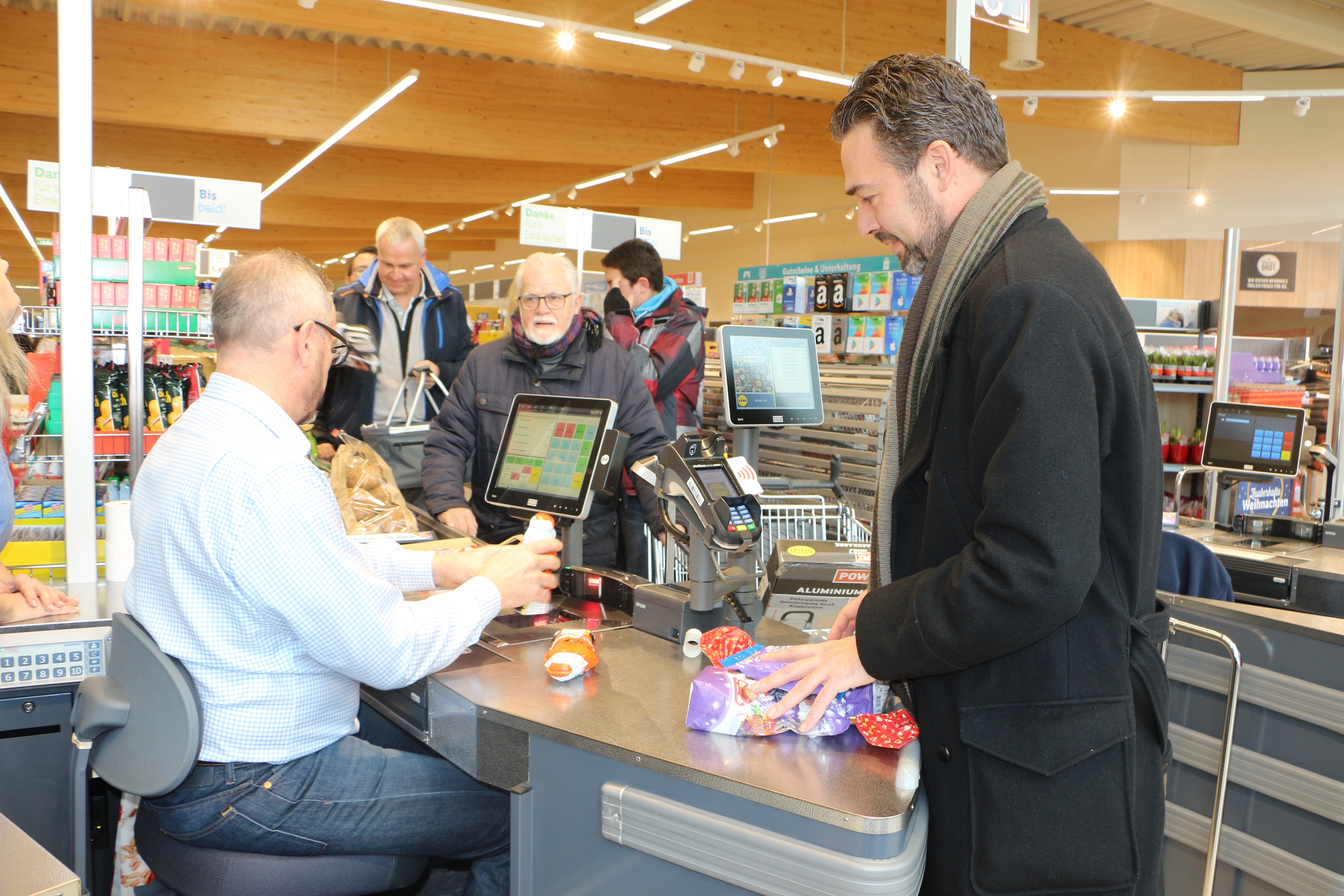 Bürgermeister Marcus Schaile (sizend) kassierte an der Lidl-Kasse. Zu den ersten Kunden gehörten Dr. Sascha Hofmann (Erster Beigeordneter) sowie Friedel Rentschler (Ortsvorsteher von Sondernheim).