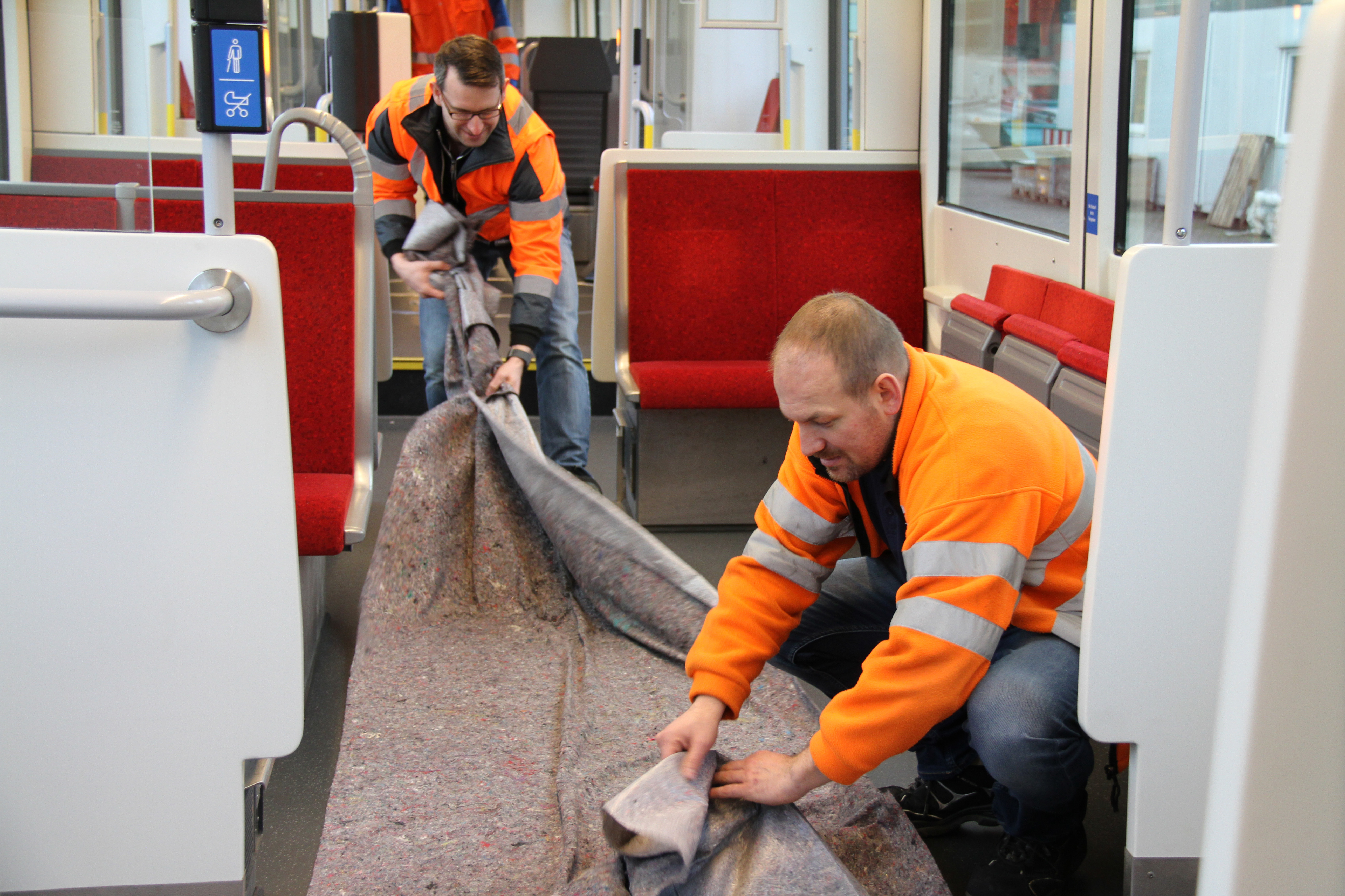 Modernisierung ihrer Fahrzeugflotte: AVG-Projektleiter Alexander Reiz (vorne) und sein Kollege Patrick Armbruster (hinten) entfernen das Schutzvlies vom neu verlegten Boden in einer modernisierten Mittelflur-Bahn