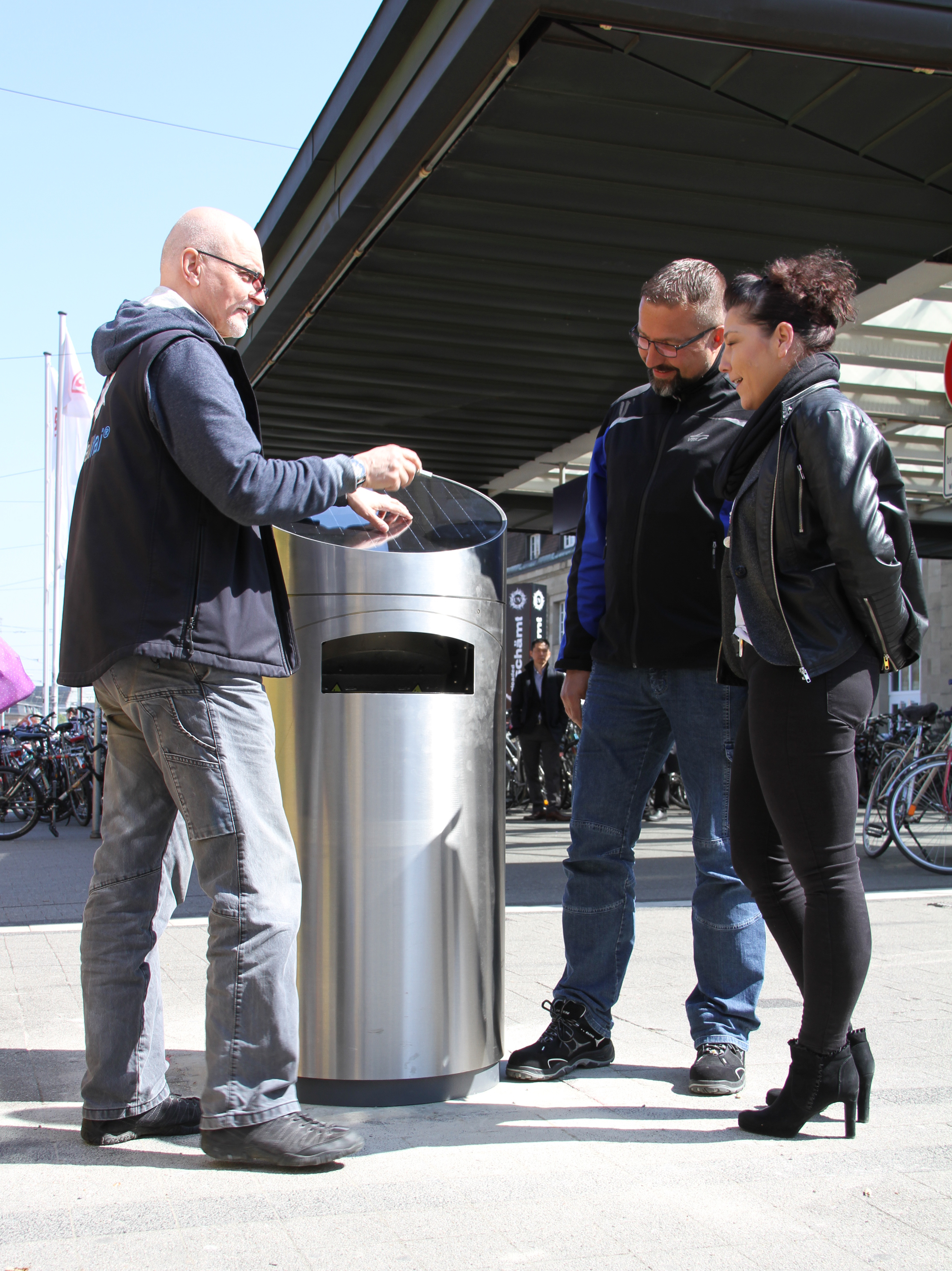 Mit dem Solar-Presshai erproben die VBK und das Amt für Abfallwirtschaft einen neuen High-Tech-Abfallsammelbehälter. Das erste Exemplar wurde heute am Karlsruher Hauptbahnhof aufgestellt. Charles Knecht (l.) von der Abfallhai Deutschland GmbH erklärt Stefan Oberacker (Mitte) von der VBK-Bahnmeisterei und AfA-Projekt- und Bezirksleiterin Nicole Schmidt (r.) die Funktionsweise des Müllverdichters