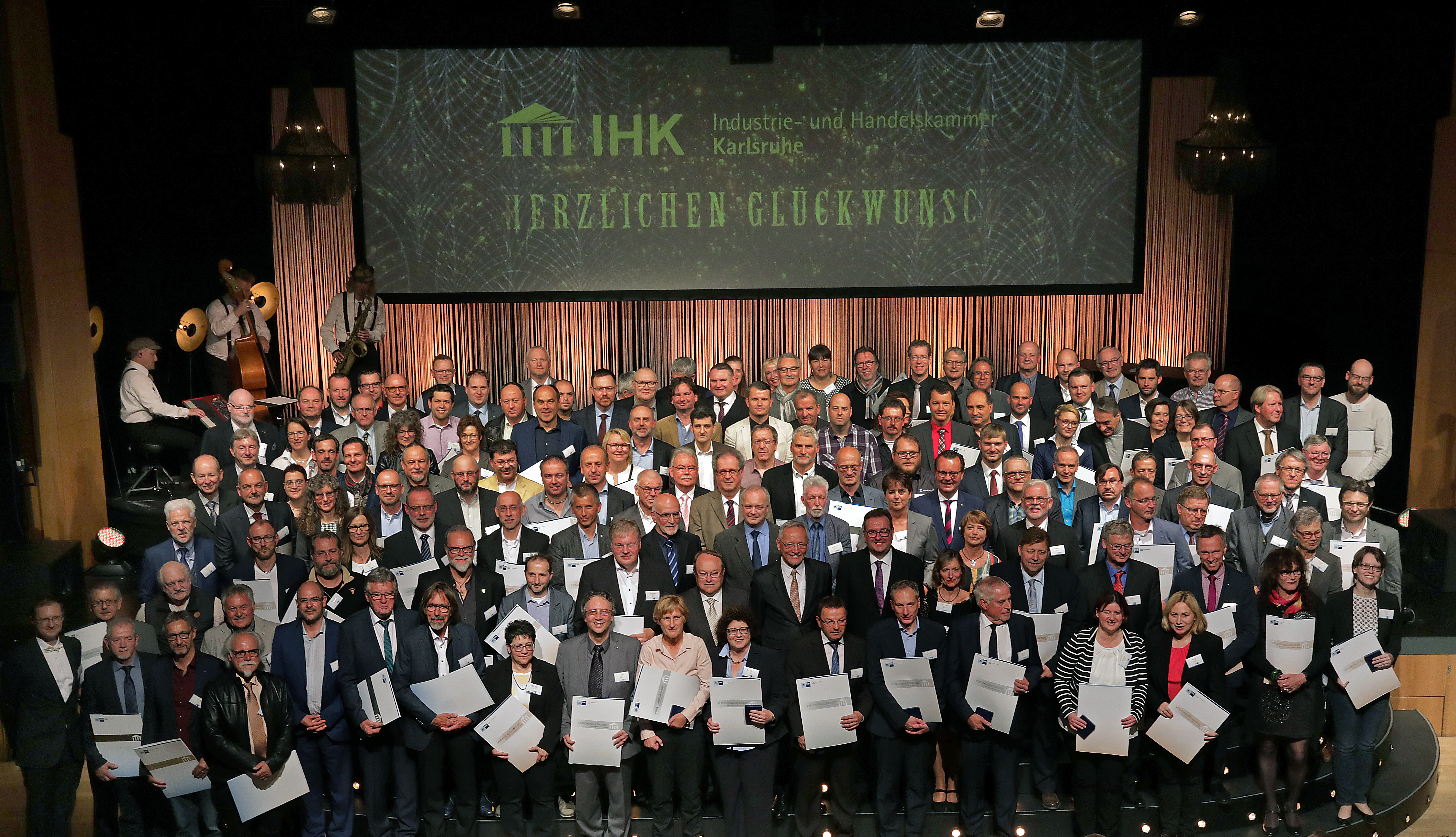 Abschlussfoto aller geehrten Prüfer gemeinsam mit IHK-Präsident Wolfgang Grenke (2. Reihe, Mitte), IHK-Hauptgeschäftsführer Dr. Guido Glania (1. Reihe, 1.v.l.) sowie Alfons Moritz, stellv. IHK-Hauptgeschäftsführer (2. Reihe, Mitte).
