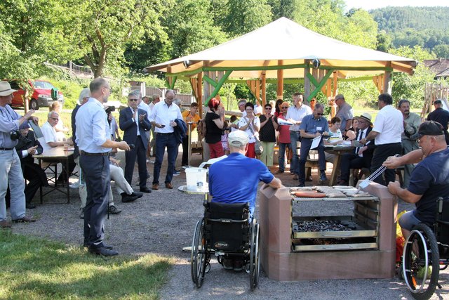 Am barrierefreien Grillplatz erfährt die Bundeskommission um den Vorsitzenden Reinhard Kubat (5. v. r. mit Hut) von Ortsbürgermeister Ralf Weber (im Vordergrund links) mit welchem ehrenamtlichen Engagement auch dieses Projekt in Rumbach umgesetzt wurde.