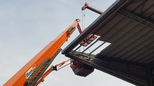 Eine Lücke im Dach ist schon da. Seit Dienstag, 6. August 2019, läuft der Abbau/Abriss der Gegentribüne des Wildparkstadions in Karlsruhe. Es ist ein aufwändiges Verfahren: Mehrere Kräne stehen an der Tribüne, einer reicht sogar direkt darüber, Arbeiter in Schutzkleidung (Asbest) zerlegen auf dem Dach dieses vor Ort zunächst Platte für Platte. Ein Container wird mit einem Kran an die Arbeitsstelle hochgehoben, dort werden die Platten dann abgelegt. Ist der Container voll, geht's damit wieder runter, dann werden die Platten umgeladen, besonders verpackt - und dann geht der Sondermüll zur Deponie.  | Foto: jnb