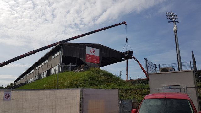 Seit Dienstag, 6. August 2019, läuft der Abbau/Abriss der Gegentribüne des Wildparkstadions in Karlsruhe. Es ist ein aufwändiges Verfahren: Mehrere Kräne stehen an der Tribüne, einer reicht sogar direkt darüber, Arbeiter in Schutzkleidung (Asbest) zerlegen auf dem Dach dieses vor Ort zunächst Platte für Platte. Ein Container wird mit einem Kran an die Arbeitsstelle hochgehoben, dort werden die Platten dann abgelegt. Ist der Container voll, geht's damit wieder runter, dann werden die Platten umgeladen, besonders verpackt - und dann geht der Sondermüll zur Deponie.  | Foto: jnb