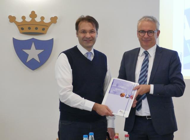 Landrat Dr. Christoph Schnaudigel (rechts) übergibt die Baugenehmigung für den Neubau der Mensa, die von Schülern der Erich-Kästner-Schule und der Ludwig Guttmann Schule gemeinsam genutzt wird, an Bürgermeister Frank Burkard (links).