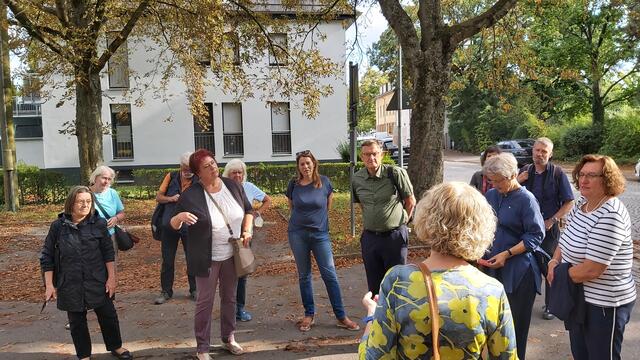 Historisch interessierte Gesellschaft vor der Informationstafel der Stadt. Silvia Scharna erläutert die Geschichte, im Hintergrund links knapp hinter dem Baumstamm sichtbar, Reste der zum Schloss Rüppurr gehörenden Mühle, der zweite Zeuge der Vergangenheit dessen.