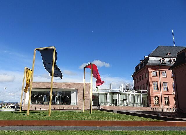 Blick auf das Restaurant "Rheintisch" des Landtages in Mainz, welches vom SV Deutschland betrieben wird. Rechts halb im Schatten liegt das Deutschhaus.

Der Anbau ist sehr modern. Die drei Fahnen in Schwarz-rot -Gold oder ähnlich sind recht salominsch aufgestellt, weil so alle Farbkombinationen gegeben sind. Nur mich erinnern sie an Bettwäsche auf der Stange. | Foto: Maiken Liefeith