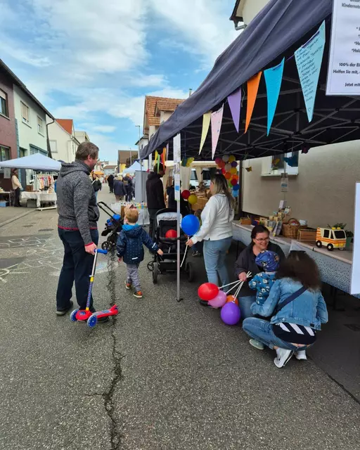 Mehrere Besucherinnen und Besucher sind zu sehen, die am Infostand des Vereins Pro Kindertagespflege Vorderpfalz stehen. Einige Menschen betrachten die bereitliegenden Informationsmaterialien, andere sprechen mit den Kindertagespflegepersonen am Stand. Kinder und Erwachsene wirken interessiert und neugierig, während sie die Angebote und Details der Kindertagespflege kennenlernen, auch wird über die Spendensammlung für den Förderverein vom Kindernotarzt gesprochen. Die Atmosphäre ist lebhaft und freundlich, und es herrscht ein reger Austausch zwischen den Besuchern und den Verantwortlichen. | Foto: Angelika Schreiweis-Brezinova