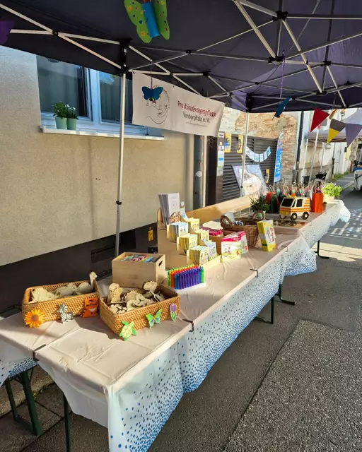 Auf dem Bild ist der Infostand des Vereins Pro Kindertagespflege Vorderpfalz zu sehen. Der Stand ist bunt dekoriert, mit Bannern und Informationsmaterial, das die Besucher über die Angebote der Kindertagespflege informiert. Mehrere Menschen, darunter Kinder und Erwachsene, stehen am Stand und schauen sich die Materialien an oder sprechen mit den Kindertagespflegepersonen. Einige Kinder sitzen an Tischen und malen, während andere neugierig um den Stand herum schauen. Die Atmosphäre ist lebendig und freundlich, und der Stand zieht viele Besucher an, die sich für die Themen rund um die frühe Betreuung interessieren. | Foto: Angelika Schreiweis-Brezinova