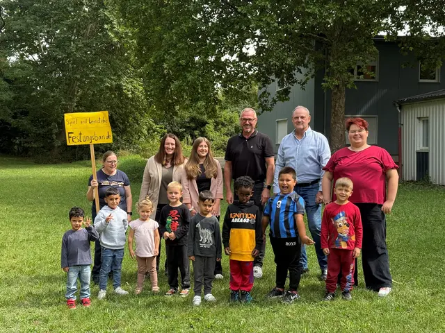 Bürgermeister Marcus Schaile (hintere Reihe, 3.v.r.), der stellvertretende Büroleiter Ludwig Hans (2.v.r.), Einrichtungsleiterin Regina Moser (ganz links, mit Schild), Veruschka Zarske (hintere Reihe, 3.v.l.), städtische Mitarbeiterin im Bereich der städtischen KITAS, sowie die beiden KITA-Mitarbeiterinnen Janine Grünsfelder (hintere Reihe, 2.v.l.) und Simone Günther (ganz rechts) freuen sich über die neuen Perspektiven, die sich nun für die Einrichtung eröffnen

 | Foto: SNelles | Stadt Germersheim | FREI