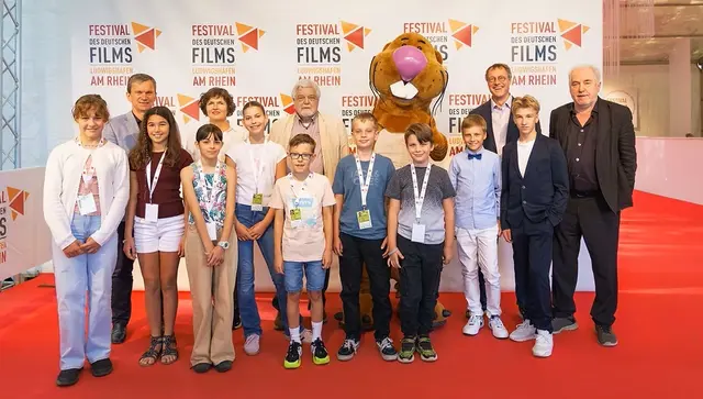 „Nils Nager“ neben Kinderfilmfestival-Kurator Rolf-Rüdiger Hamacher (mitte, hinten), Festivalintendant Dr. Michael Kötz (rechts), Programmdirektorin Daniela Kötz (links), Holger Martens, Geschäftsführer der Rheinpfalz (links, dahinter), die 7köpfige Kinderjury - Noreen Chiuia, Anna Bergner, Gilbert Himpele, Lale Wippert, Henrik Spieß, Kareem Heinrich und Aksu Erbektas – sowie Kinderfilmpreis Gewinner Norbert Lechner mit seinen beiden Hauptdarstellern Silas John und Konstantin Horn. | Foto: Festival des deutschen Films
