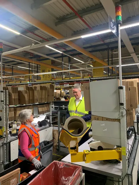 Ministerpräsident Alexander Schweitzer bekommt eine Einweisung zum Paketemachen.  | Foto: Bohlander