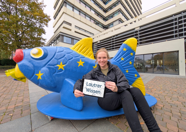 Die Projektverantwortliche Benita Becker präsentiert die neue Webplattform "Lautrer-Wissen.de" vor dem Rathaus mit dem Europafisch, eine der Fischskulpturen, die im Wissensportal verzeichnet sind | Foto: KL.Digital/gratis