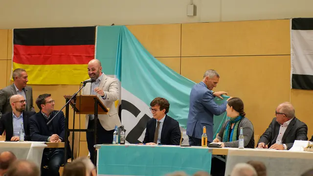 Kleiner Zwischenfall mit großer Wirkung: Als die Fahne plötzlich nachgab, sorgte Landrat Ralf Leßmeister mit geübtem Griff für Ordnung – begleitet von Schmunzeln und Applaus im Saal. | Foto: Erik Stegner