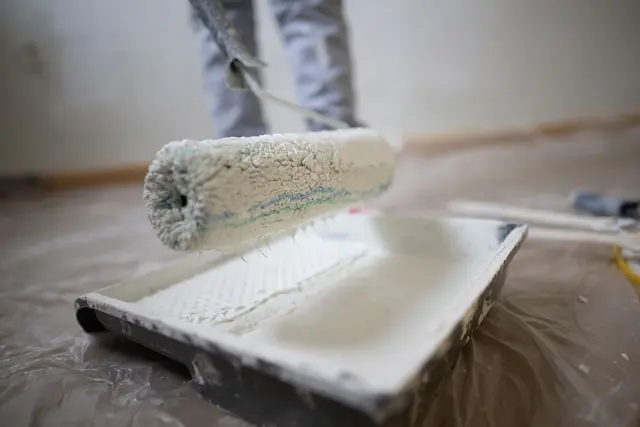 Eine Frau nimmt weiße Farbe auf, um eine Wand zu streichen. | Foto: dpa