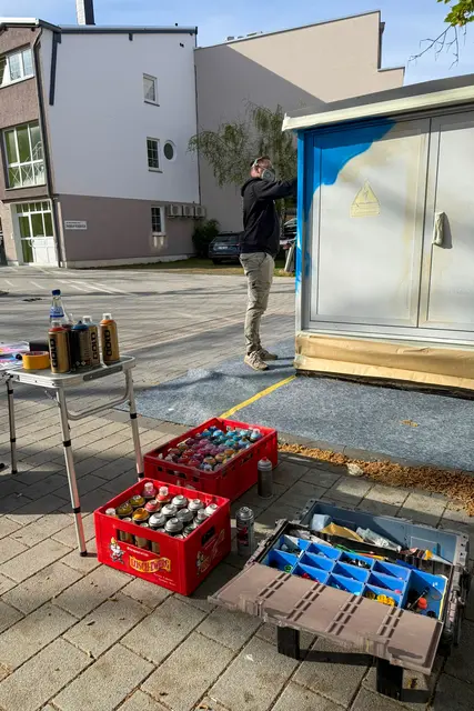 Vorbereitung für das Kunstwerk: Spraydosen, Farben und Werkzeug stehen bereit, während Daniel Ferino an der Trafostation am Adolph-Kolping-Platz die nächsten Arbeitsschritte plant. | Foto: Stadt Landstuhl