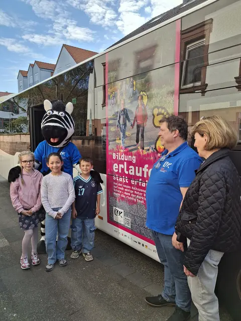 Der Bus der TWK mit dem großflächigen Traffic-Board, den Schüler*innen der Grundschule Pfaffenwoog Erfenbach, Zebra Sam, Erik Hippchen und Dr. Bettina Göbelsmann (v.l.n.r.) | Foto: Gabi Fliege