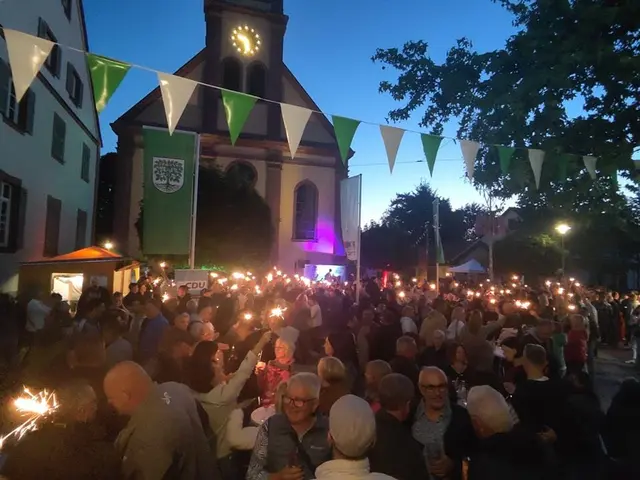 Das Bild zeigt ein Straßenfest in der Dämmerung vor einer Kirche