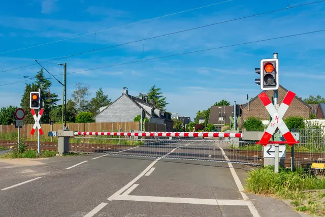 Das Bild zeigt einen Bahnübergang mit geschlossenen Schranken