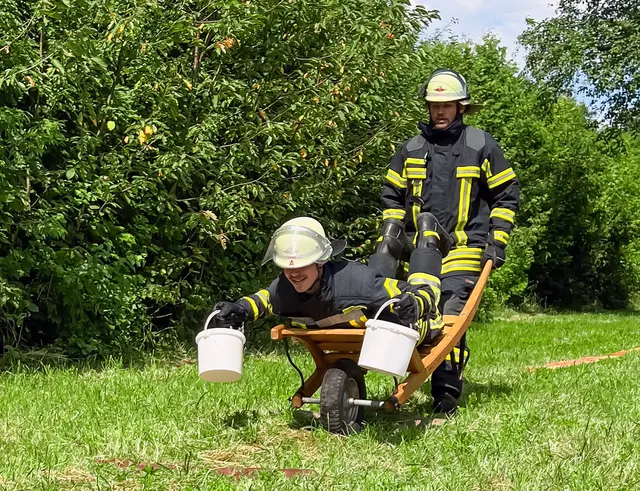 Das Team der Freiwilligen Feuerwehr Aue schiebt in voller Montur seine Schubkarre über den Hansaplatz und tritt beim Schubkarrenrennen an – Schubkarrenrennen beim Hansa-Fest in Durlach-Aue