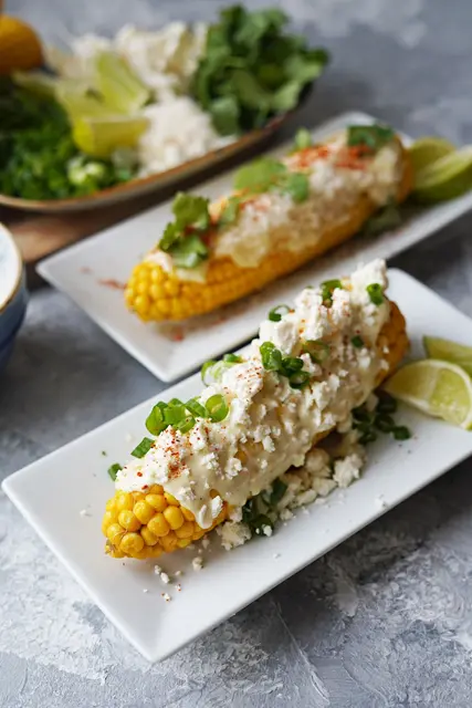 Die fertigen Maiskolben bekommen ein «Zudecke» aus selbstgemachter Mayo und Dingen, die der Kühlschrank gerade so hergibt - etwa Parmesan, Feta, Frühlingszwiebel und Rucola. (zu dpa: «Einfach, doch zugleich raffiniert: Maiskolben mit Topping») | Foto: dpa