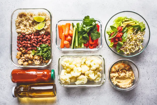 Vorbereitete Meal-Prep-Zutaten wie Gemüse, Reis, Bohnen und Dip in mehreren Behältern
