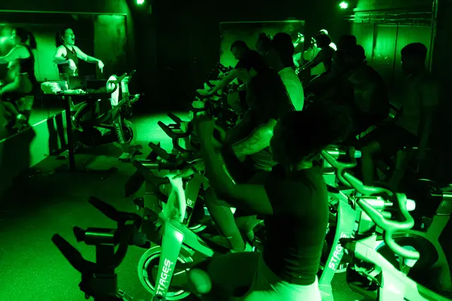 Indoor-Cycling-Kurs bei Power Cycle Studio in Kaiserslautern: Trainerin motiviert eine Gruppe von Teilnehmenden auf Spinning-Bikes in grün beleuchtetem Studioraum.