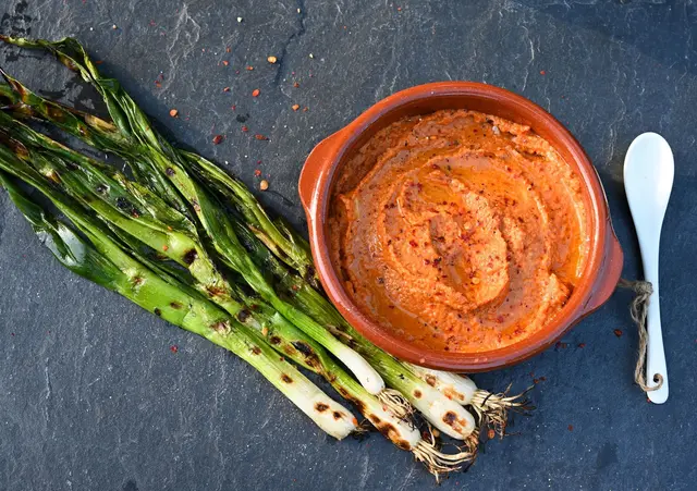 Die gegrillten Frühlingszwiebeln müssen nur noch in den katalanischen Paprika-Dip eingetunkt werden und in den Mund wandern - dann kann das Gaumenfeuerwerk starten. | Foto: Julia Uehren/dpa-mag