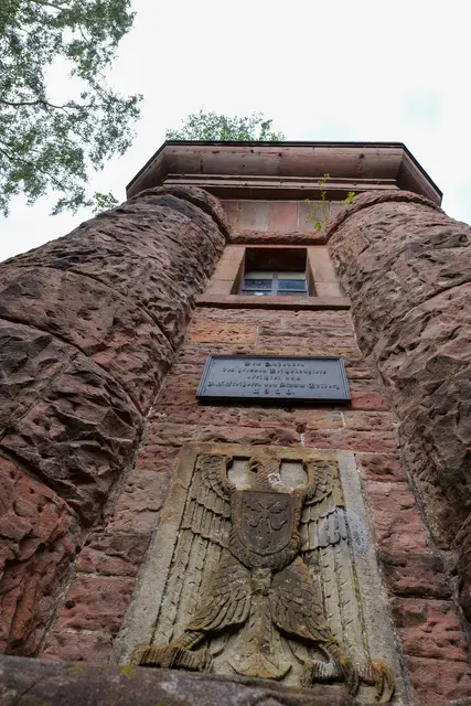 Der Blick nach oben zeigt den massiven Buntsandsteinbau des Bismarckturms. An der Fassade erinnern eine Gedenktafel und das Bismarckrelief an die Entstehung des Denkmals. | Foto: Erik Stegner