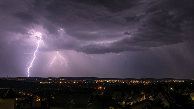 Symbolbild: Gewitter über einer Stadt bei Nacht. Der Deutsche Wetterdienst warnt am Mittwochabend in Landstuhl vor starken Gewittern mit Sturmböen, Starkregen und Hagel. | Foto: Erik Stegner mit KI