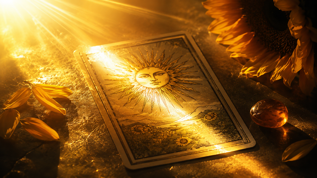 Die Tarot-Karte ‚Die Sonne‘ liegt in einem hellen, goldenen Lichtstrahl, umgeben von Sonnenblumenblättern und einem glänzenden Bernstein