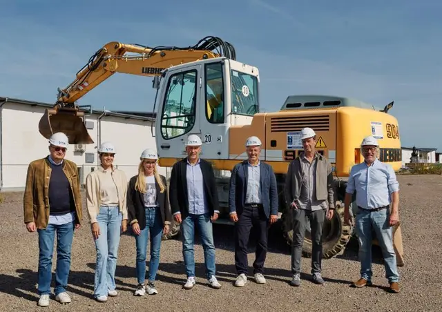 Vertreter des Zweibrücken Fashion Outlets vor einem Bagger auf der geplanten Erweiterungsfläche des Outlet-Centers.