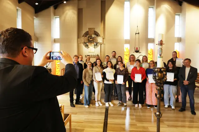 Mann fotografiert die Teilnehmenden, die ihre Vokationsurkunden halten.