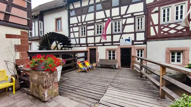 Historisches Fachwerkgebäude des Museums unterm Trifels in Annweiler mit Holzsteg, Wasserrad und Eingang zum Museum.