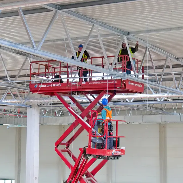 In luftiger Höhe arbeiten Monteure an den technischen Installationen unter dem Hallendach. Der Innenausbau der neuen Elis-Großwäscherei schreitet weiter voran. | Foto: Erik Stegner