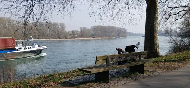 An der Rheinpromenade in Speyer gibt es das komplette Set für Frühlingsentspannung: ruhiges Wasser, ein gemächlich vorbeiziehendes Frachtschiff und ein Mensch, der offenbar beschlossen hat, sich direkt auf der Parkbank seinen ganz persönlichen Urlaubsort einzurichten.
Eines kann man mit Sicherheit sagen: In Speyer versteht man es, die einfachen Freuden des Lebens zu schätzen – ein wenig Sonne, der Blick auf den Fluss und eine Bank, die sich plötzlich in eine Liege der Businessklasse verwandelt. | Foto: Liubov Arnold